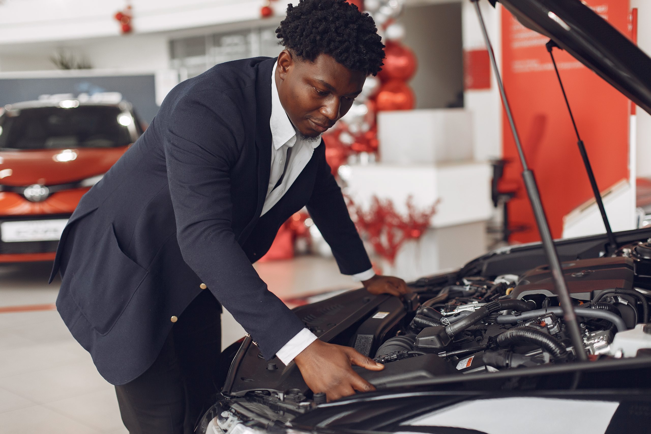 Man buying the car. Businessman in a car salon. Black male in a suit.